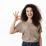 All under control. Smiling young woman assure everything OK, showing okay sign and say yes, approve or agree, recommend good thing, praise nice work, standing over white background.